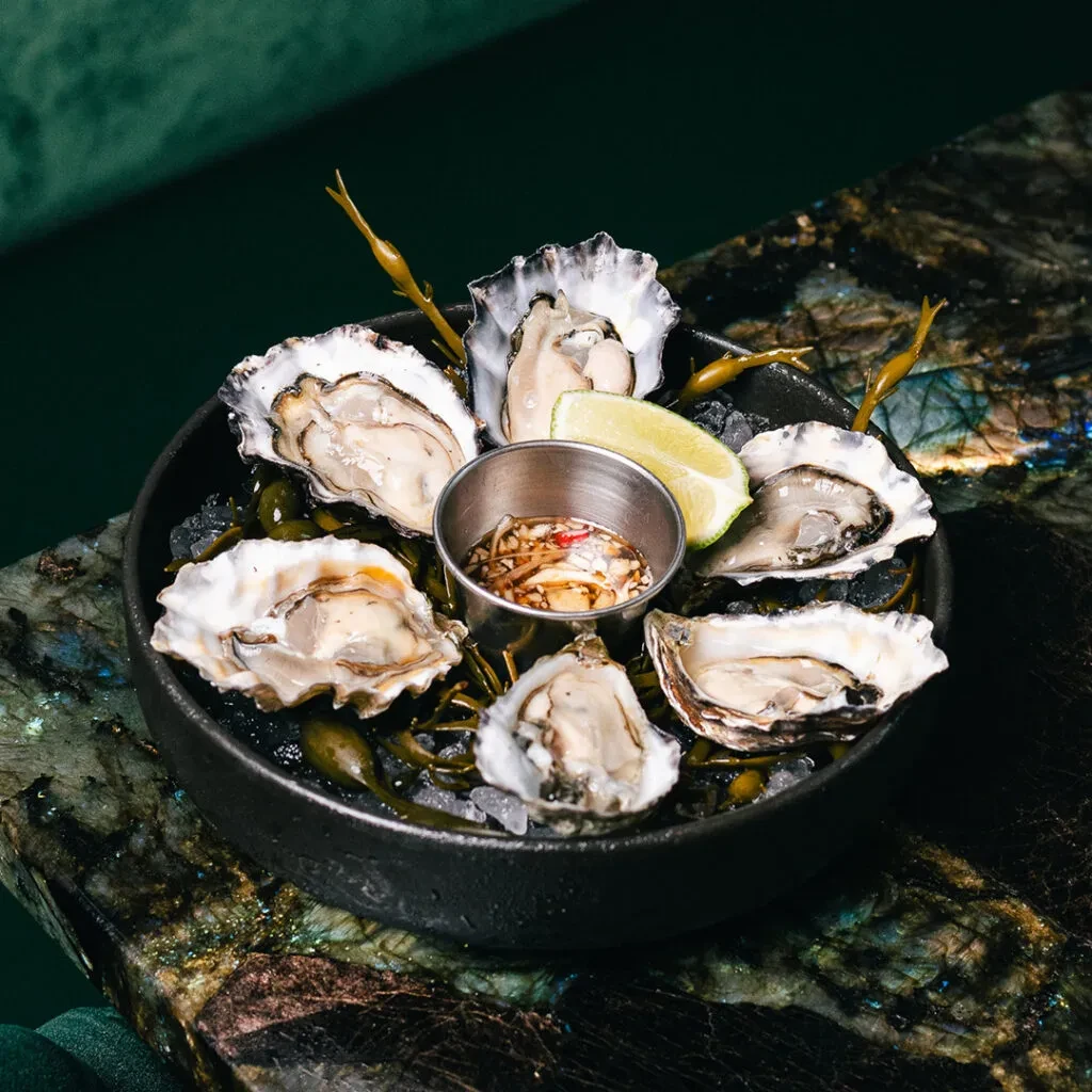 Fresh shucked oysters on ice with dipping sauce and lime.