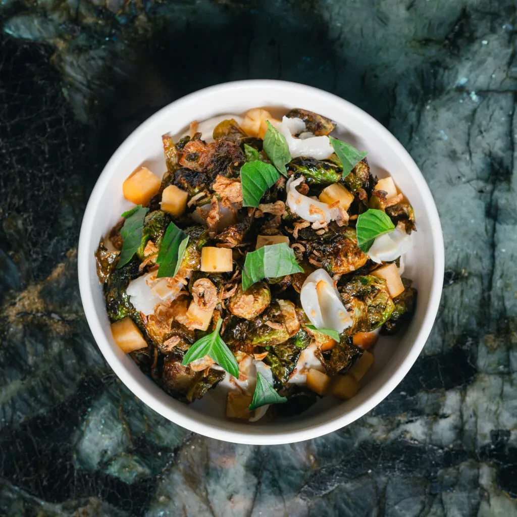 Dish of roasted Brussels sprouts, mango, coconut, basil, and fried shallots.
