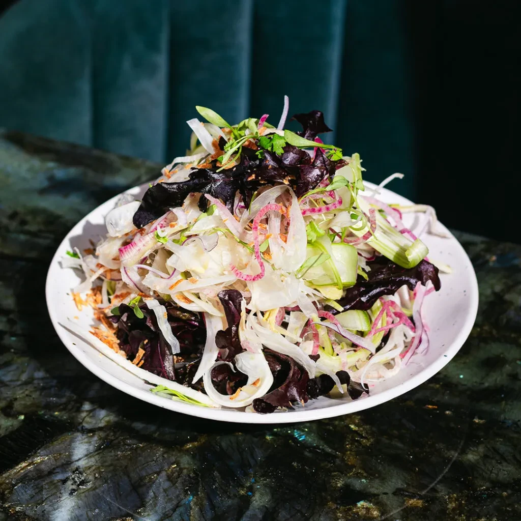 Colorful fresh salad in a white bowl on a dark reflective surface.