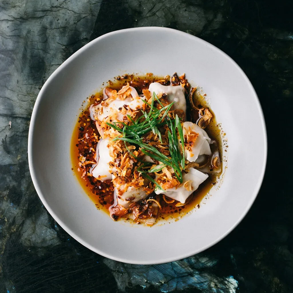 Spicy dumplings in chili oil sauce with fried shallots and fresh herbs.