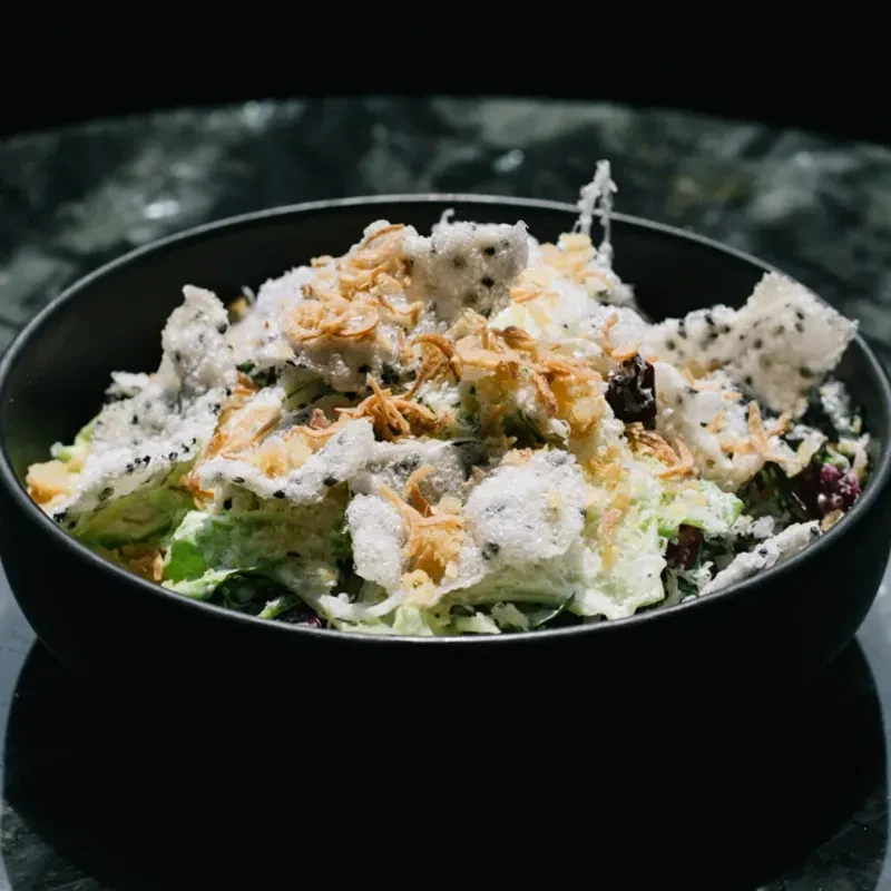 Vibrant salad with creamy dressing, crisps, and fried shallots in dark bowl.