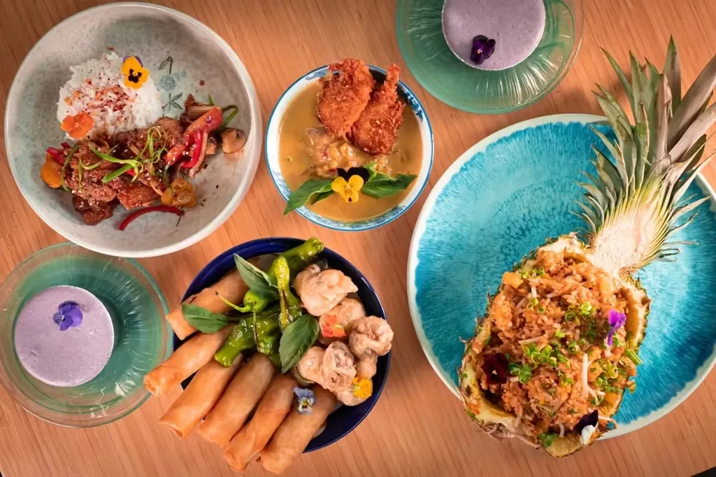 Overhead: colorful Asian food spread with purple drinks.