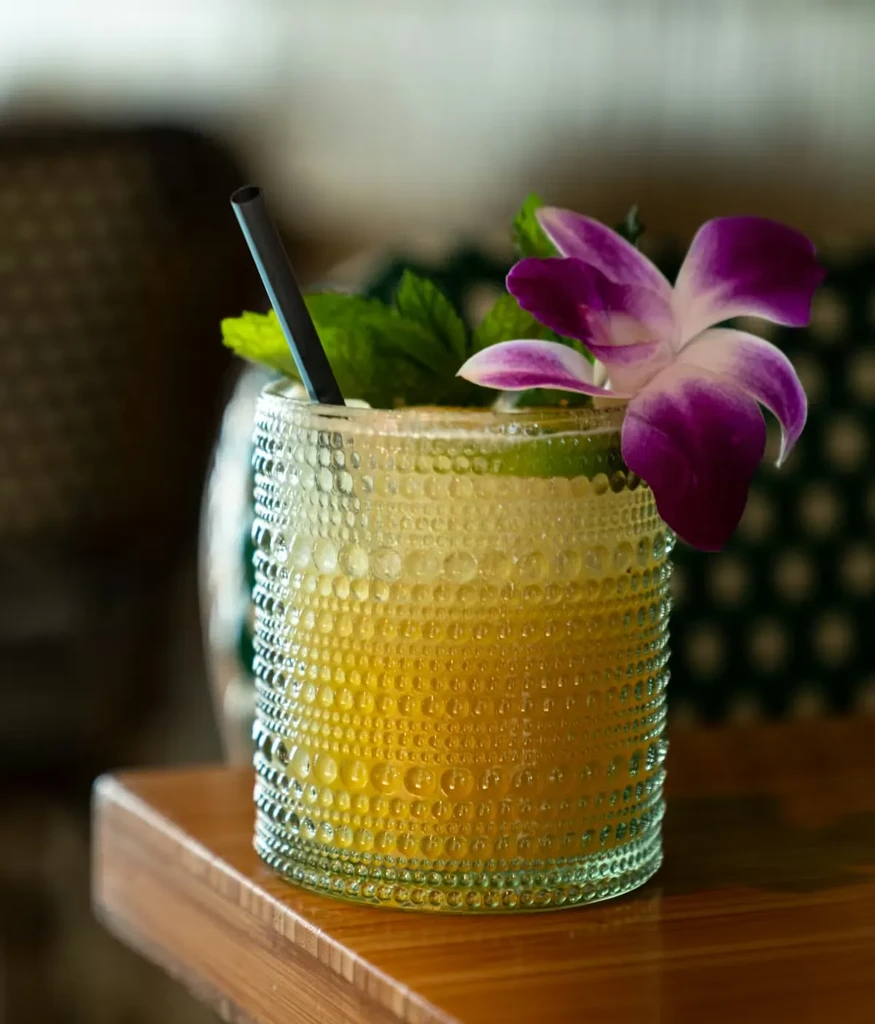 Cocktail in bobbled glass with mint, purple orchid, and straw.