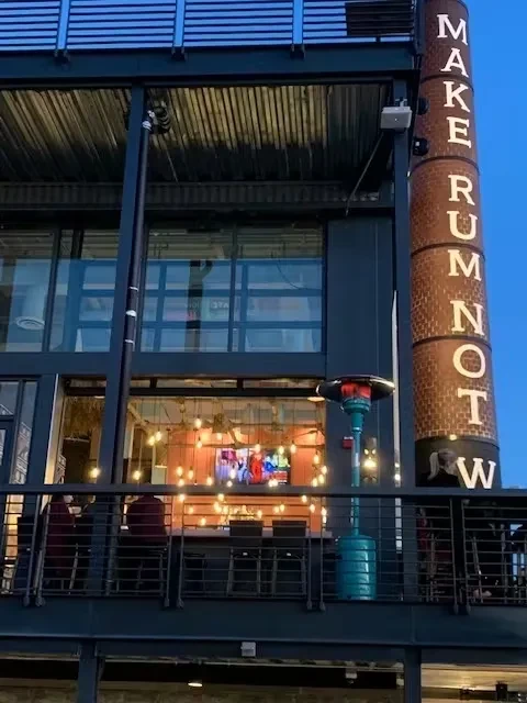 Modern restaurant at dusk with "MAKE RUM NOT WAR" sign.