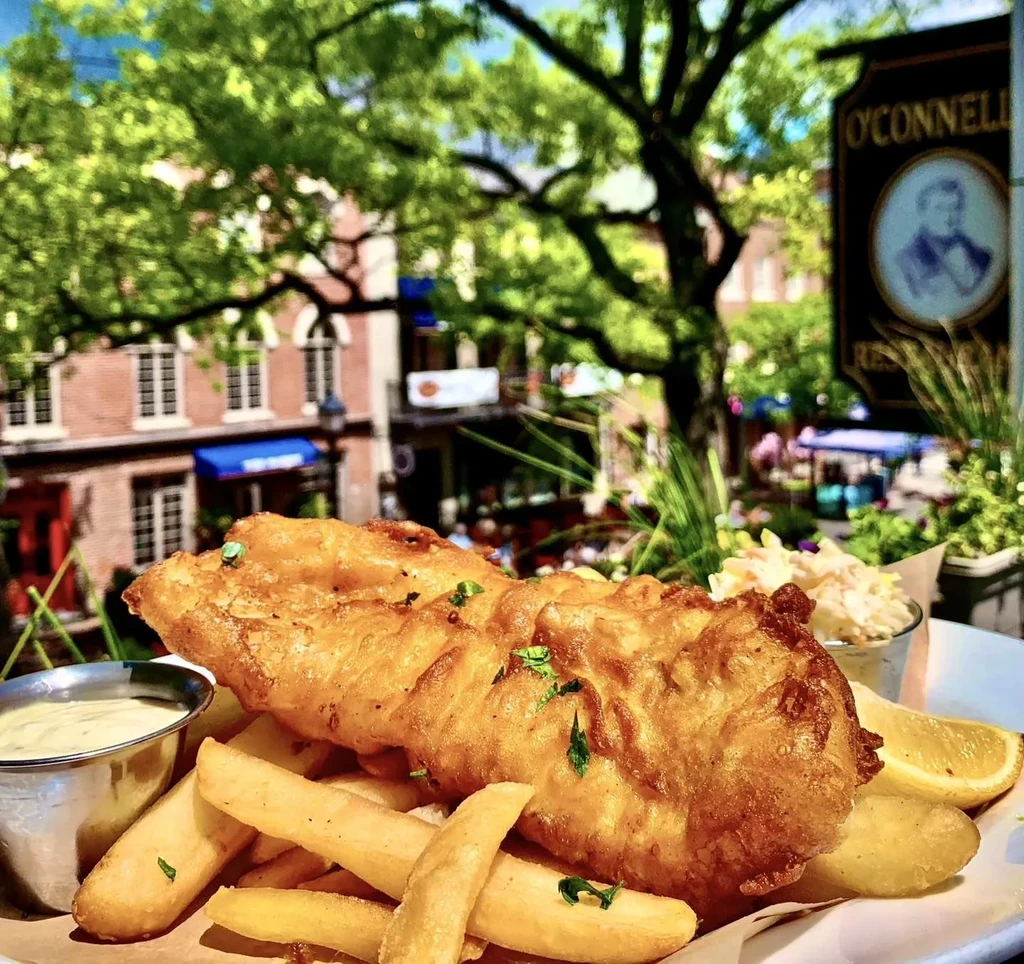 Golden fish and chips with coleslaw, lemon, and sauce, served outdoors.