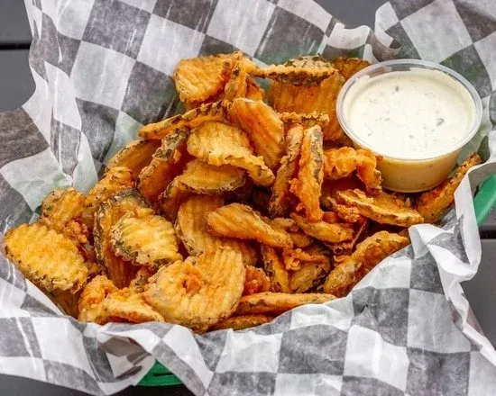 Golden brown fried pickles in a green basket with creamy dipping sauce.