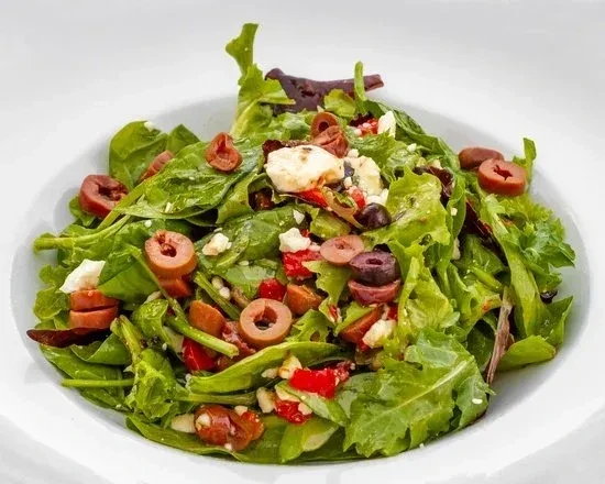 Colorful salad with greens, olives, feta, and red peppers in white bowl.