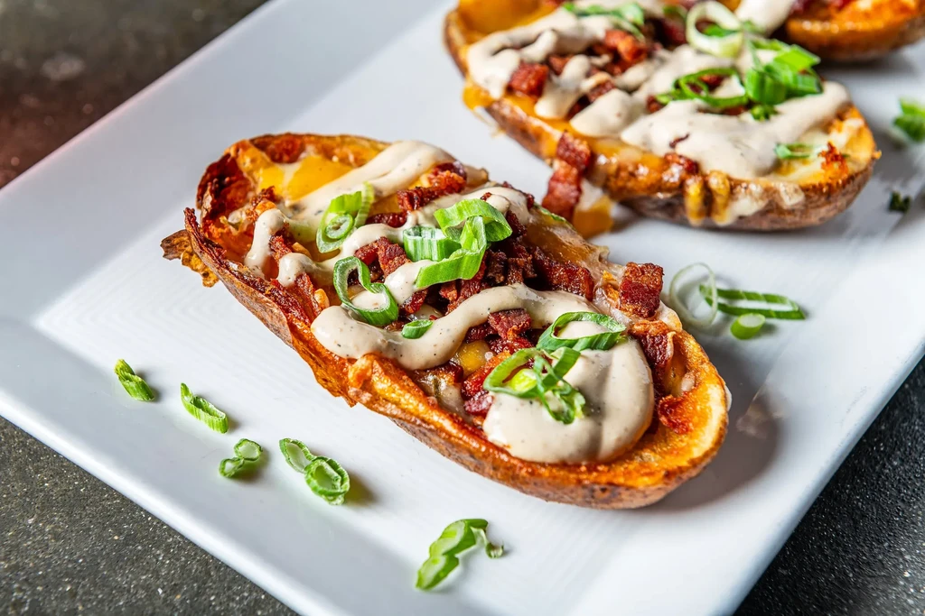 Potato skins topped with melted cheese, bacon, sauce, and green onions.