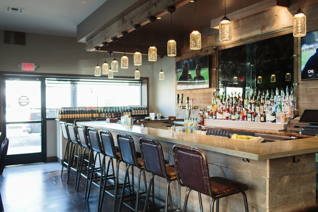 Modern bar interior with long counter, stocked liquor display, and TVs.