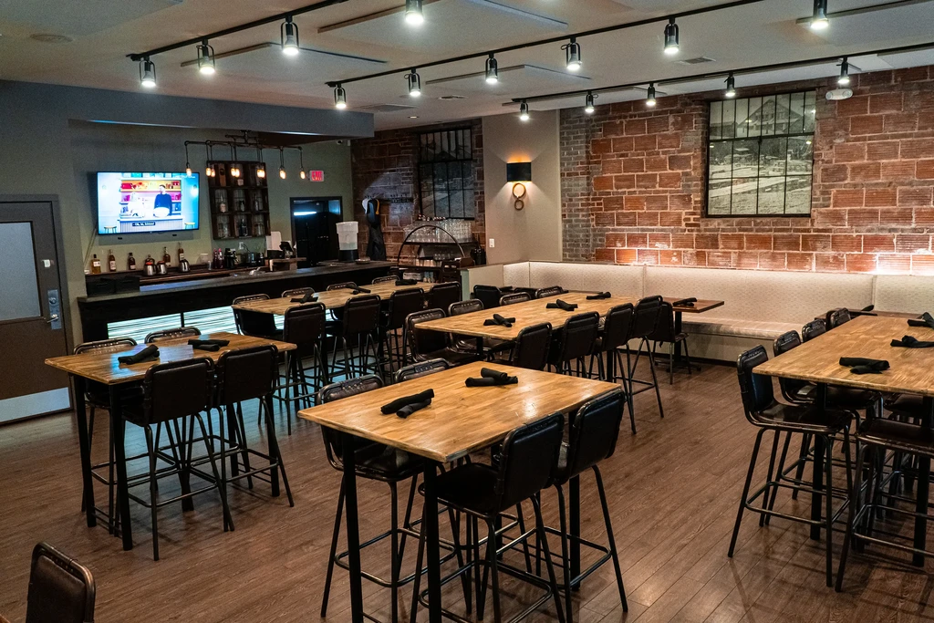 Modern restaurant interior: high-top tables, long bar, exposed brick.