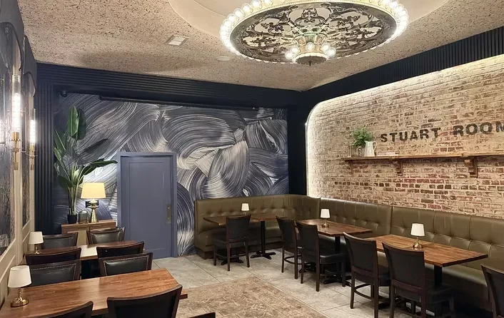 Restaurant's 'Stuart Room' with brick wall, green booth, and chandelier.