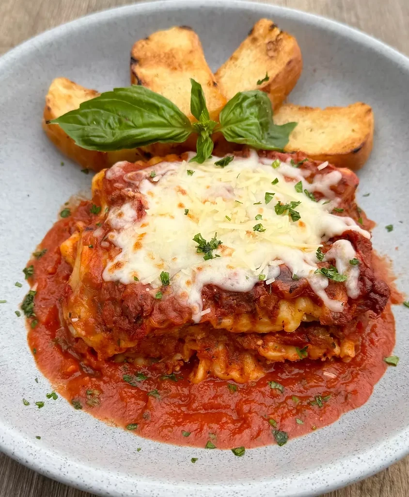 Lasagna with red sauce, melted cheese, basil leaves, and toasted bread.