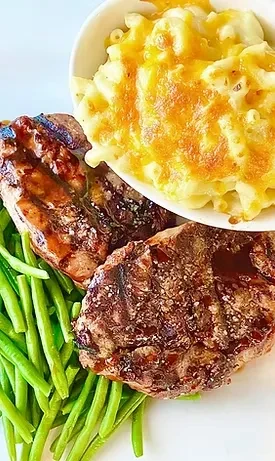 Plated meal: mac and cheese, glazed meat portions, and green string beans.