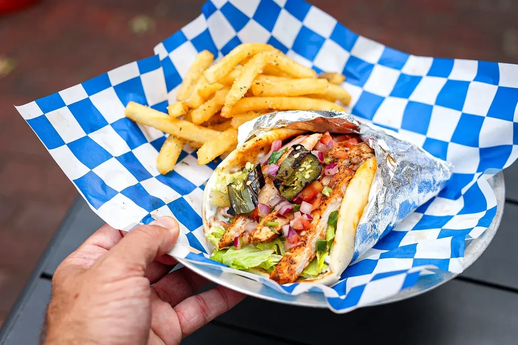 Hand holding grilled chicken wrap with jalapeños and fries.
