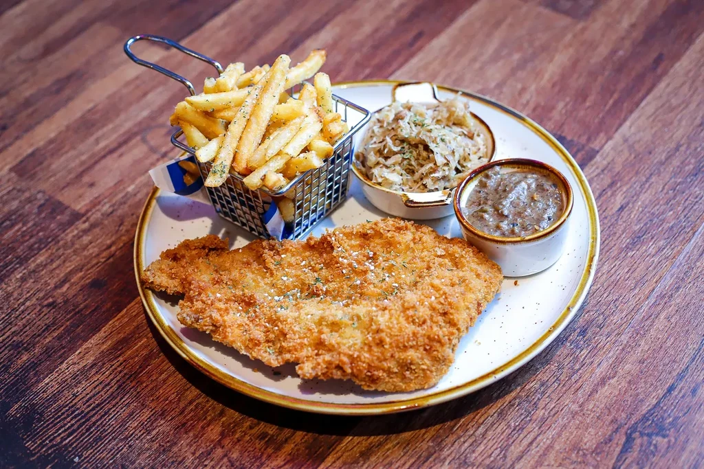 Golden breaded cutlet, fries, sauerkraut, and gravy on a wooden table.