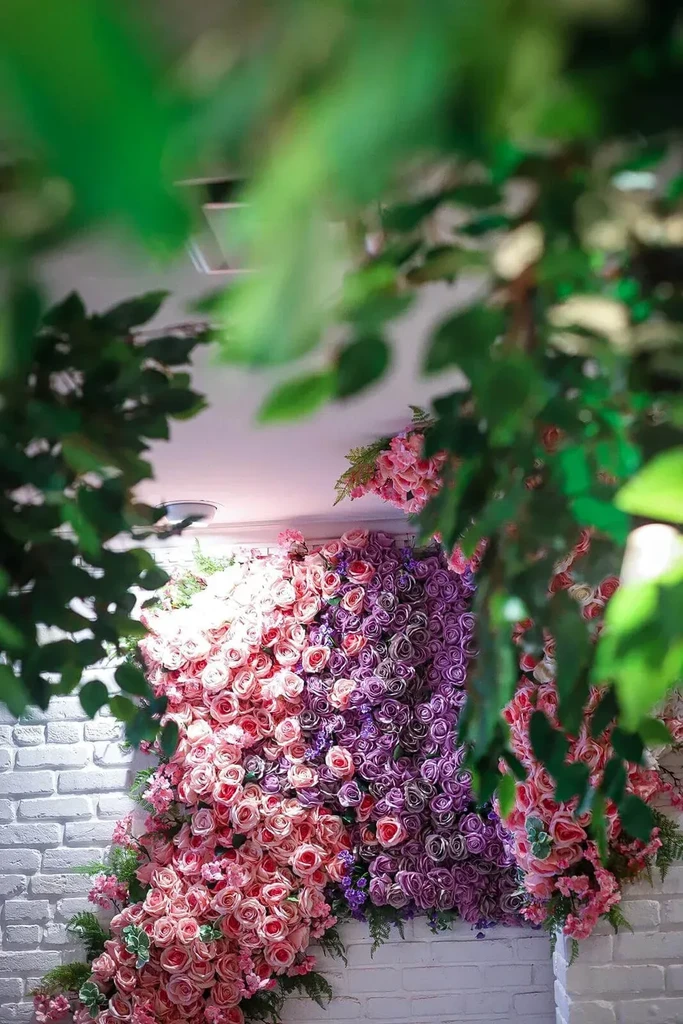 Bright wall of pink and purple artificial roses on brick.
