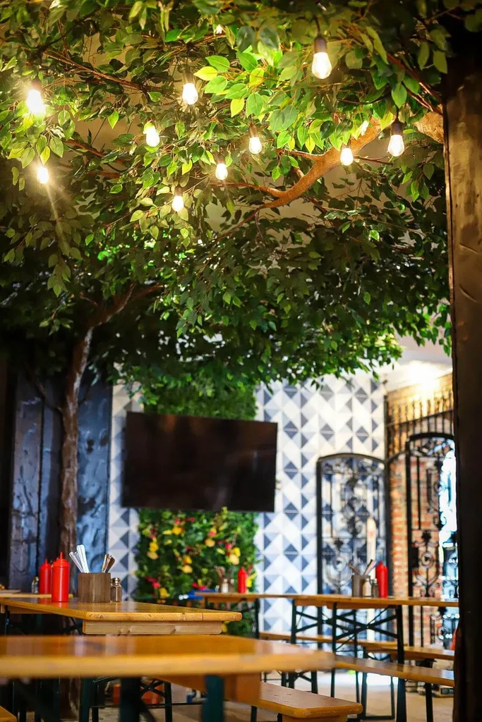 Casual restaurant interior with artificial tree canopy and string lights.