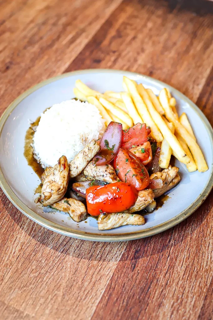 Plate of stir-fried chicken, rice, and fries on a wooden table.
