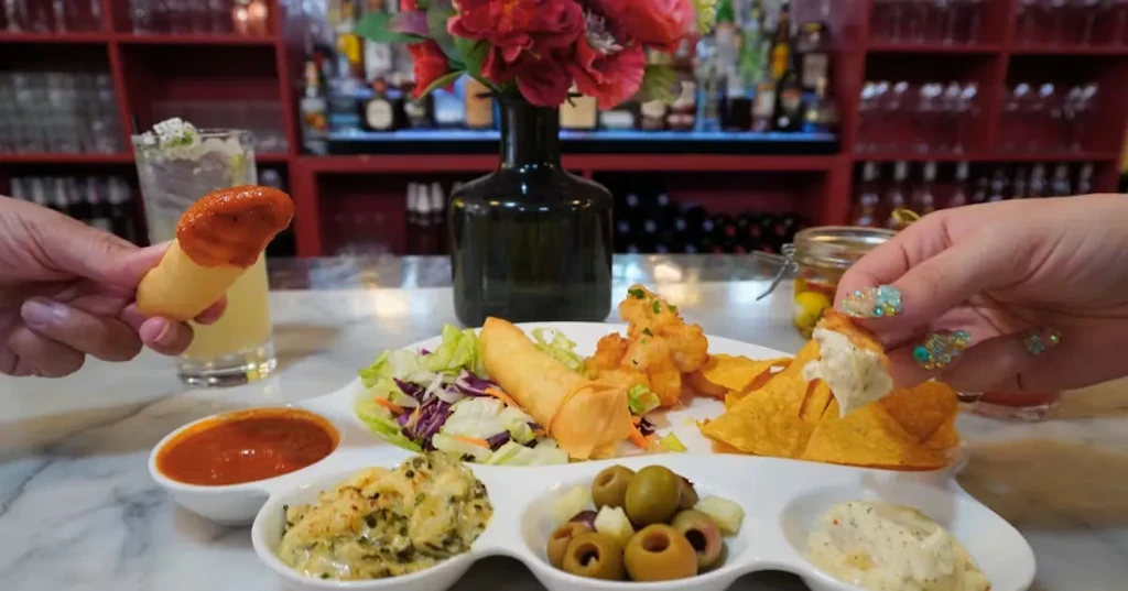 Hands eating appetizers and drinks on a marble table at a bar.