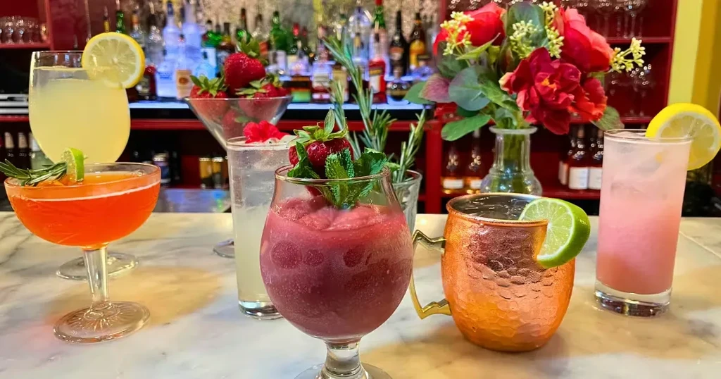 Six colorful cocktails and beverages on a bar counter.
