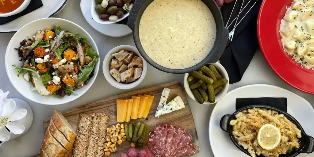 Overhead table of fondue, salad, charcuterie, pasta, and mac and cheese.