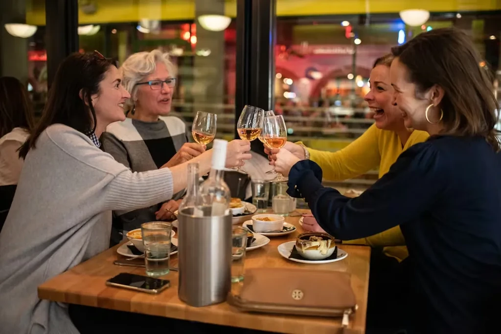 Four women smiling, toasting with rosé wine in a restaurant.