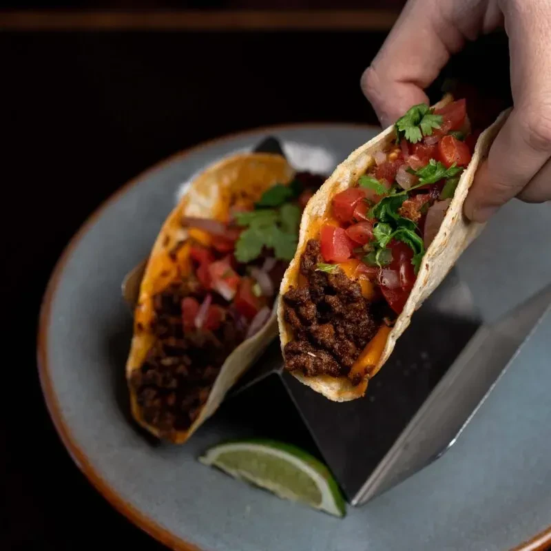 Soft-shell tacos with seasoned meat, cheese, tomatoes, cilantro; one held.
