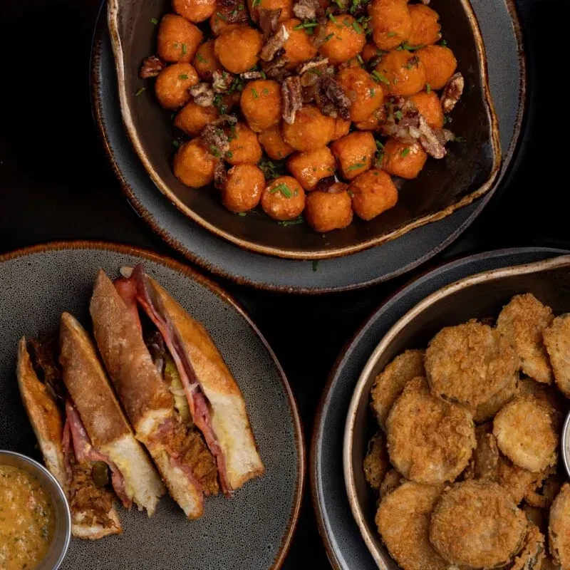 Three food dishes: gnocchi with nuts, pressed sandwich, and fried pickles.