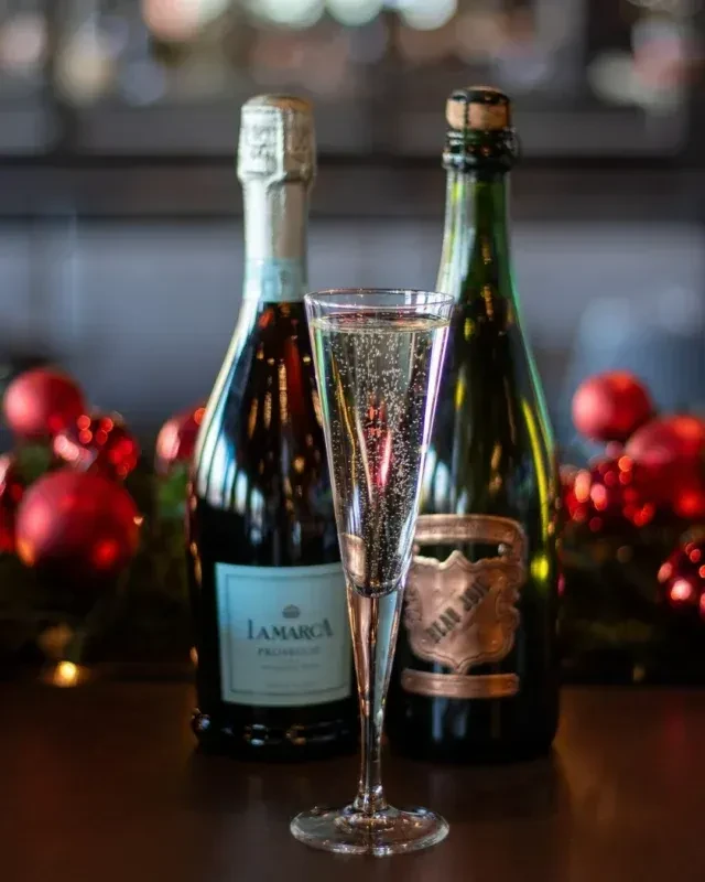 Sparkling wine in flute, two bottles, and blurred festive background.