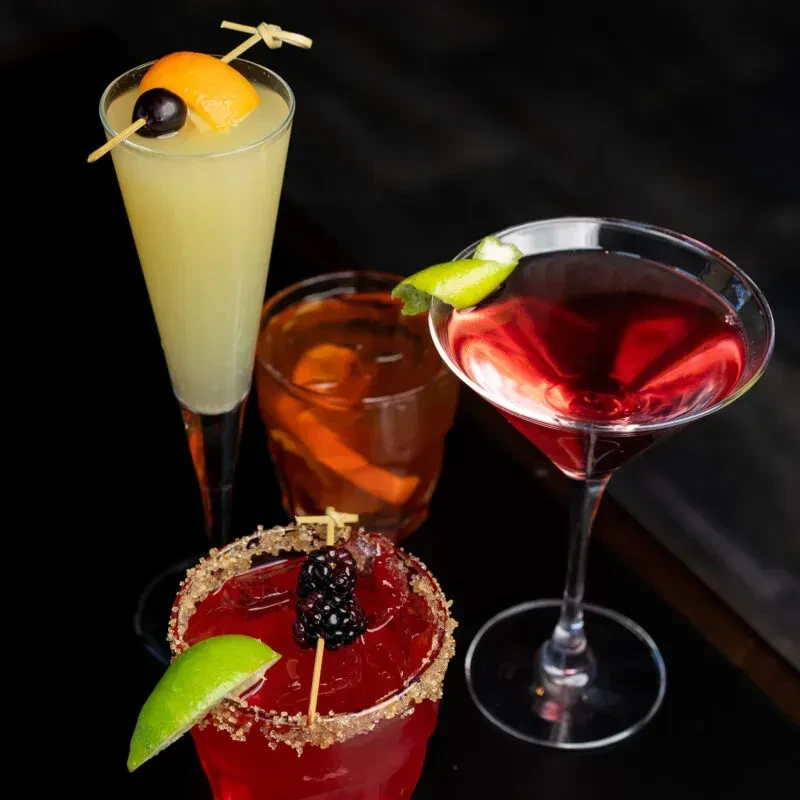 Four unique cocktails with various garnishes on a dark background.