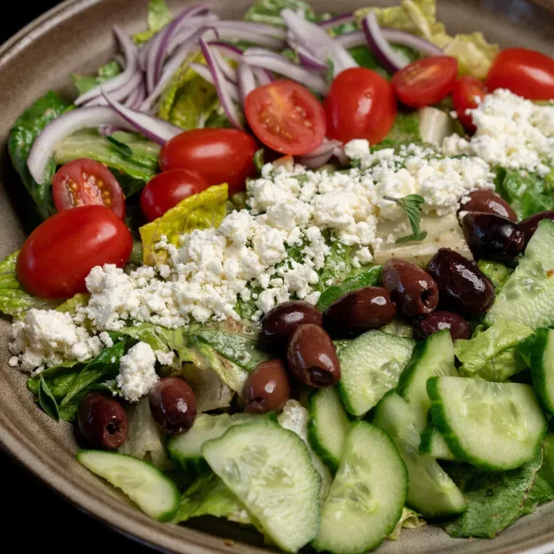 Vibrant Greek salad in a brown bowl with feta and olives.