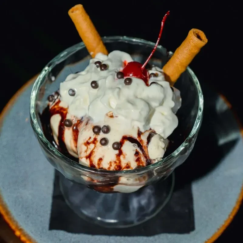 Vanilla sundae with chocolate sauce, whipped cream, cherry, and wafer rolls.