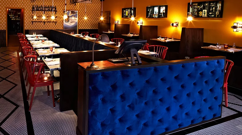Empty restaurant with red chairs, blue counter, and golden patterned walls.