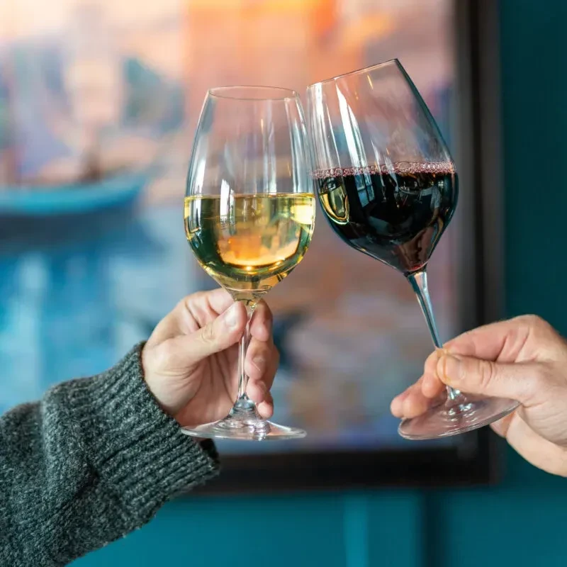 Hands clinking glasses of white and red wine.