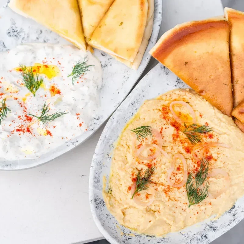 Appetizer plates of hummus and tzatziki with pita, dill, and spice.