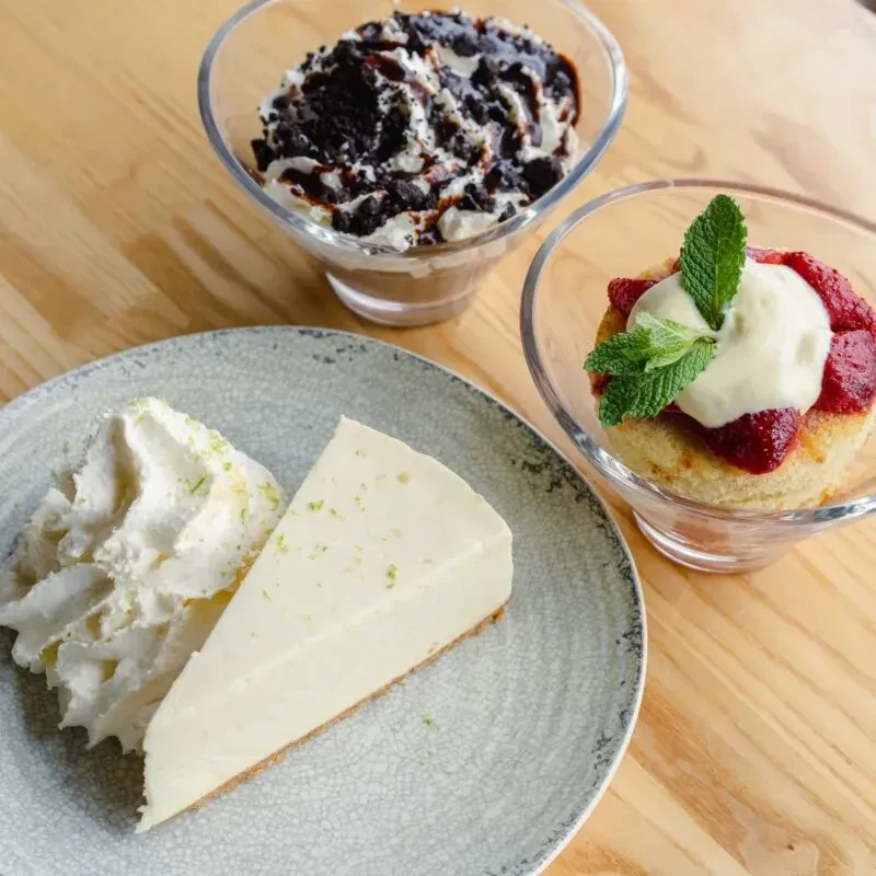 Three desserts: cheesecake, chocolate cookie parfait, and fruit trifle on wood.