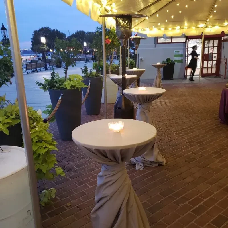 Outdoor evening patio with candlelit tables, fairy lights, and distant boardwalk.