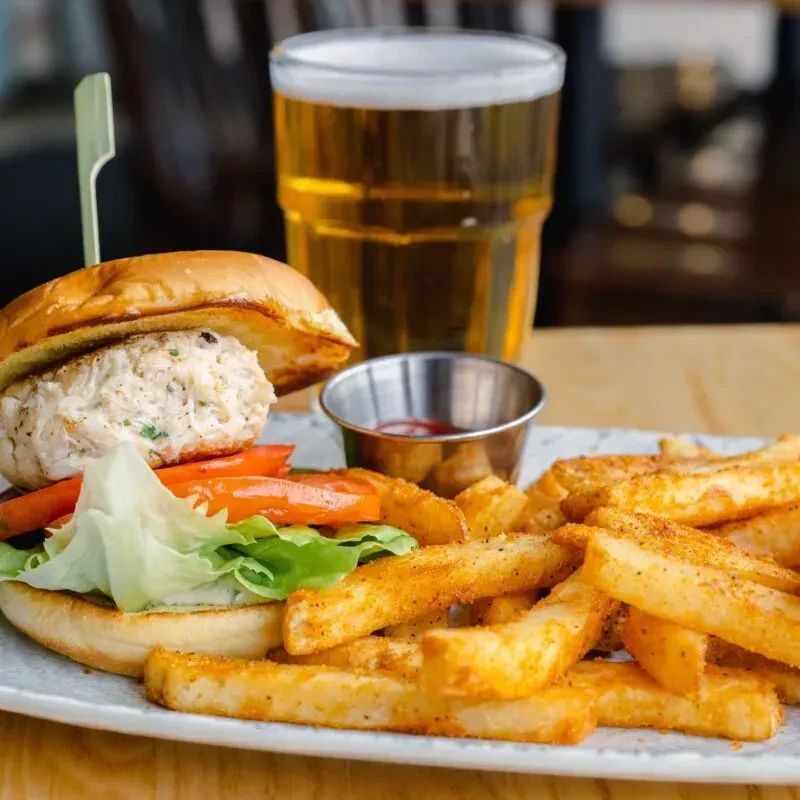 Open-faced crab cake sandwich, french fries, ketchup, and beer.