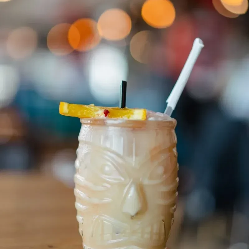 Tiki cocktail in idol glass, garnished with orange slice and two straws.