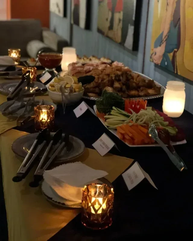 Warmly lit buffet table with appetizers, vegetables, and a red dipping sauce.