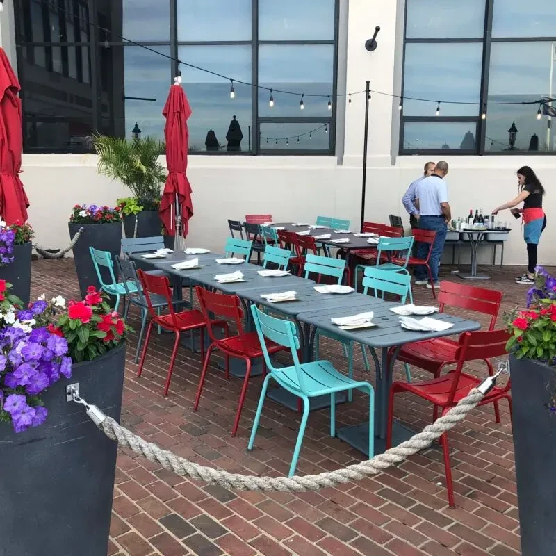 Outdoor patio with red and teal chairs, tables, plants, umbrellas.