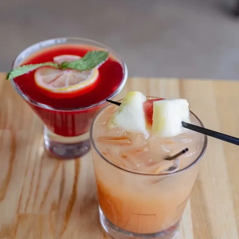 Orange drink with pineapple and red drink with mint on table.
