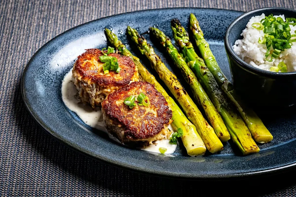 Plated pan-seared patties with asparagus, rice, and green onions.
