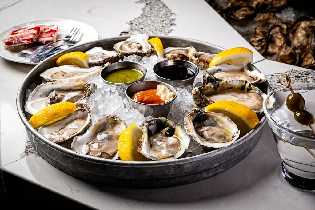 Rustic platter of fresh oysters on ice with lemon, sauces, and cocktail.