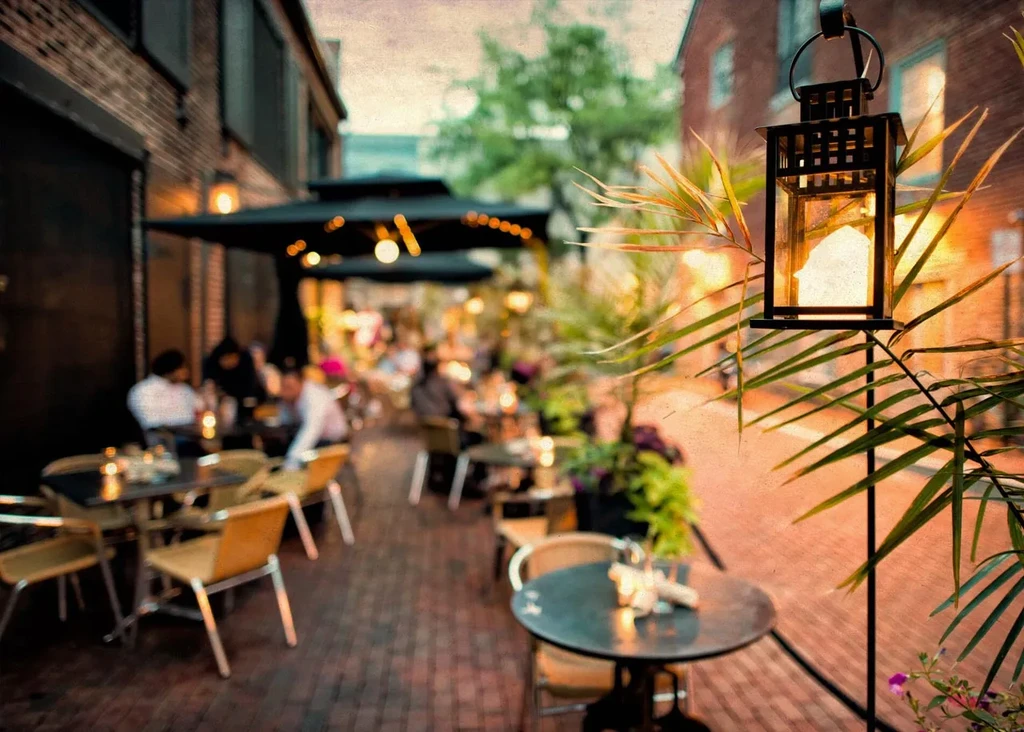 Warmly lit outdoor restaurant patio with glowing lantern and blurred patrons.