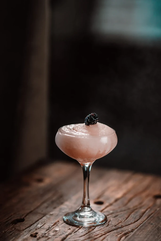Frothy pink cocktail with blackberry garnish on rustic wood.