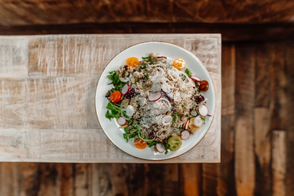 Colorful salad bowl with greens, tomatoes, radishes on a rustic table.
