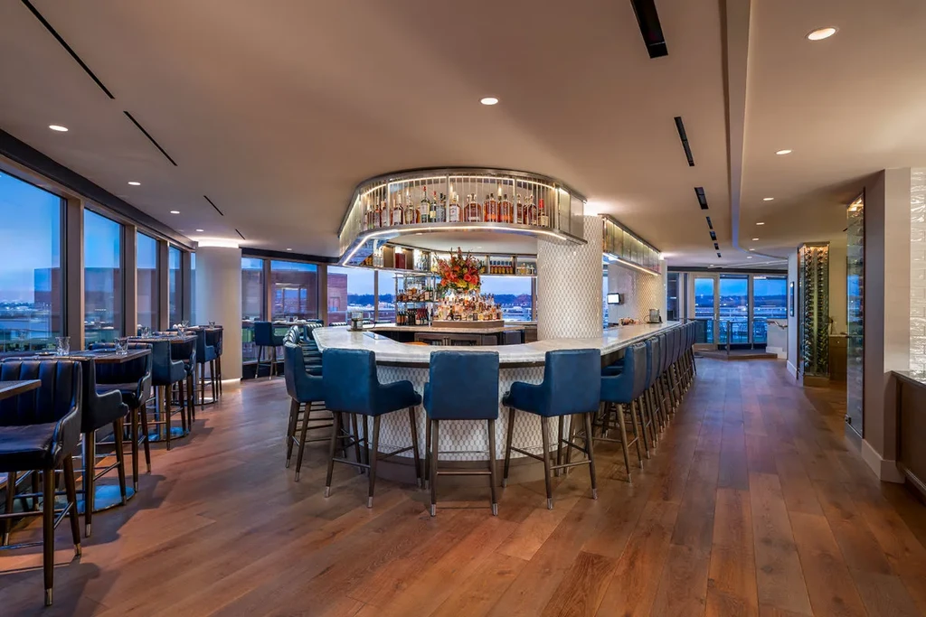 Empty upscale bar with marble counter, blue stools, and city view.
