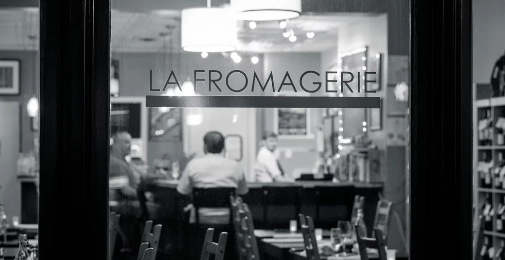 Black and white photo of LA FROMAGERIE restaurant interior through glass.