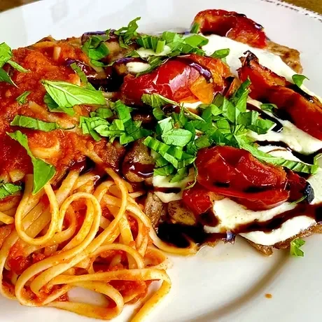 Plated pasta with red sauce, chicken, cheese, tomatoes, basil, glaze.